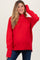 woman wearing a red turtleneck maternity sweater and blue jeans, smiling and touching her hair