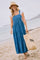 woman wearing a denim tiered maxi dress with a white t-shirt underneath and a straw hat, holding a beach bag on the sand