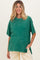 woman wearing a green oversized maternity t-shirt with short sleeves and a relaxed fit, posing with one hand in pocket