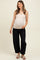 woman wearing a light beige maternity tank top, black wide-leg jeans, and showing her baby bump