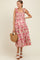 woman wearing a pink floral maternity maxi dress with tie straps and a smocked bodice, holding a straw handbag