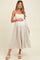 woman wearing a light beige maternity dress with spaghetti straps and a flowy silhouette, holding her baby bump
