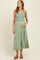 woman wearing a light green maternity dress with ruffled straps, smocked bodice, and button details, holding her baby bump