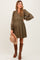 woman wearing an olive green maternity dress with button details and embroidered long sleeves, holding a beige hat