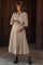 woman wearing a beige tiered maternity dress with a tie waist and three-quarter puff sleeves, holding her baby bump