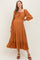 woman wearing a rust-colored maternity dress with long sleeves and tiered skirt, showcasing her baby bump