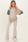woman wearing a beige maternity sweater with green and striped sleeves and light beige flared pants, showing her baby bump
