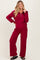 woman wearing a burgundy maternity athletic set with a zip-up sweatshirt and wide-leg pants, posing with one hand on her hip