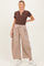 woman wearing a brown ribbed maternity henley top and beige wide-leg maternity pants, standing with a smile