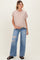 woman wearing a light pink maternity top and distressed wide-leg jeans, holding her baby bump