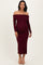 woman wearing a burgundy off-the-shoulder maternity dress, showcasing her baby bump, with long sleeves and a fitted silhouette