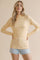 woman wearing a yellow long sleeve top with floral print and a scalloped neckline, paired with denim shorts