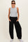 woman wearing a gray sleeveless top and black wide-leg maternity pants, standing with hands in pockets