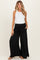 woman wearing a white tank top and black wide-leg maternity pants with a drawstring waist and side pockets