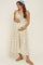 woman wearing a cream floral maternity dress with adjustable straps and a gathered waist, holding her baby bump