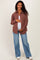 woman wearing a rust plaid maternity button-up shirt and blue flared jeans, holding her baby bump