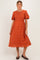 woman wearing a rust-colored maternity dress with puff sleeves and floral embroidery, standing against a light background