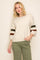 woman wearing a cream oversized sweater with green and brown striped sleeves and olive green pants