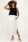 woman wearing a black knitted maternity top and a beige maxi skirt with a side slit, posing with one hand on her hip