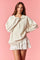 woman wearing an oversized cream pullover sweatshirt paired with a white ruffled mini skirt