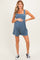 woman wearing a denim blue maternity romper with smocked bodice and holding her baby bump