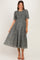 woman wearing a grey floral maternity dress with short puff sleeves and a smocked bodice, standing and smiling