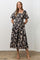 woman wearing a black floral midi dress with puff sleeves and a smocked bodice, standing with hands in pockets
