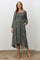 woman wearing a dark green floral mid-length dress with long sleeves and pockets, styled with strappy heels
