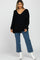 woman wearing a black oversized v-neck sweater with long sleeves and blue wide-leg jeans, standing in a relaxed pose