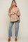 woman wearing a beige maternity top with button detailing, holding her baby bump, paired with distressed jeans and tan mules