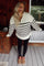woman wearing a white and black striped zip-up sweater with leggings and cozy slippers, smiling indoors