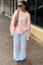 woman wearing a light pink oversized sweater, striped wide-leg pants, and sunglasses, standing outside.