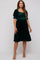 woman wearing a dark green velvet maternity dress with short puff sleeves and a smocked bodice, featuring a ruffled hemline