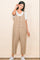 woman wearing a beige linen jumpsuit with buttons and side pockets over a white t-shirt and white sneakers