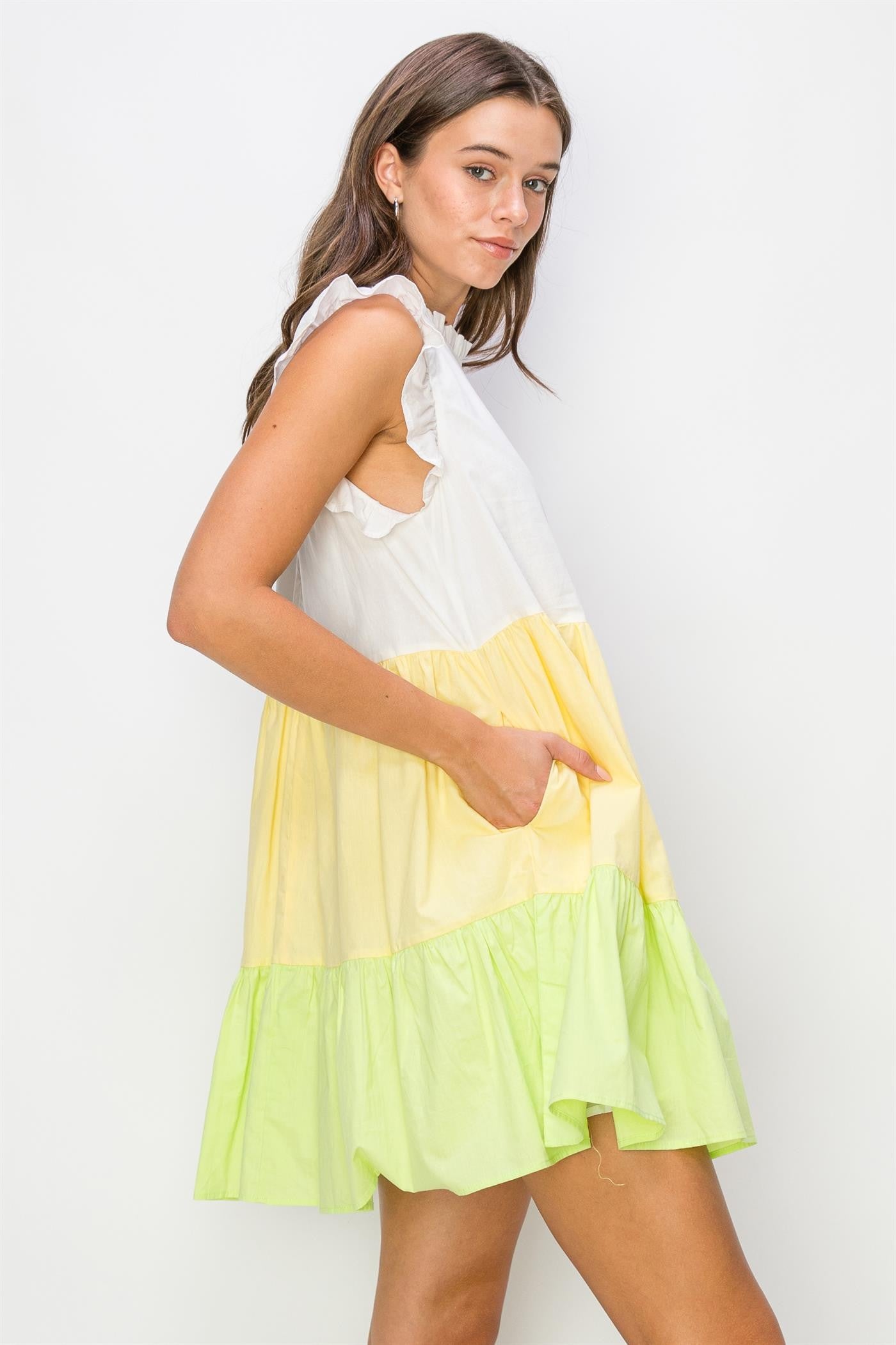 woman wearing a sleeveless color-blocked dress with white, yellow, and green tiers and ruffled details