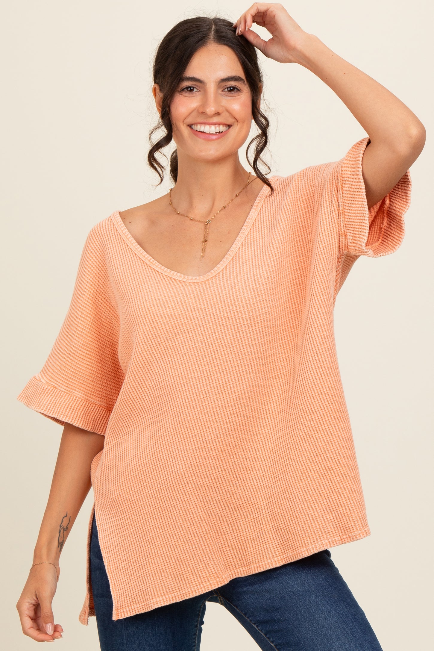 woman wearing a coral oversized knit top with short sleeves and a v-neck, smiling against a neutral background