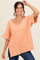 woman wearing a coral oversized knit top with short sleeves and a v-neck, smiling against a neutral background