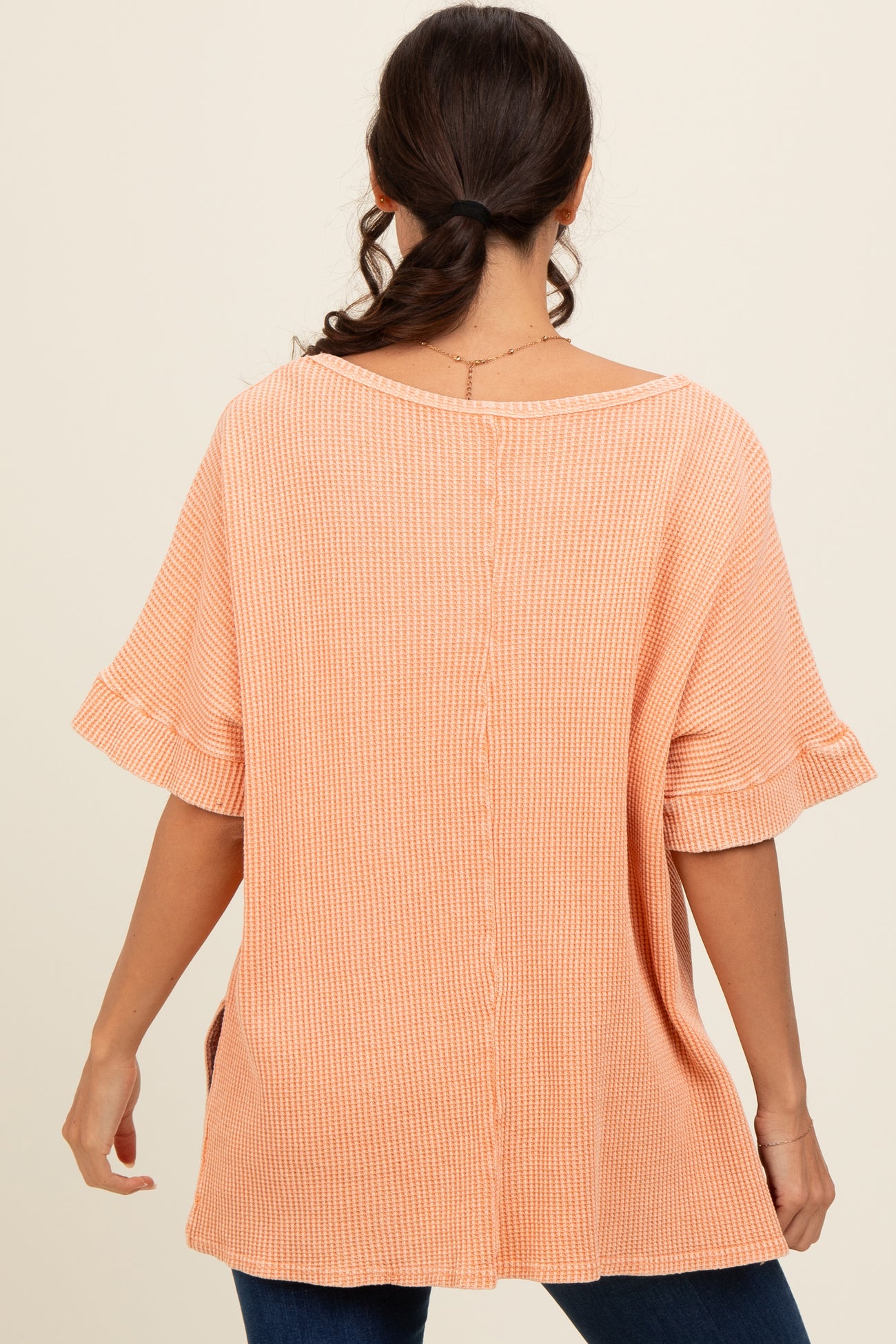 woman wearing a peach ribbed oversized top with short ruffled sleeves and a button detail running down the back