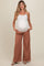 woman wearing a white maternity camisole and rust-colored wide-leg pants, showing her baby bump with hands in pockets