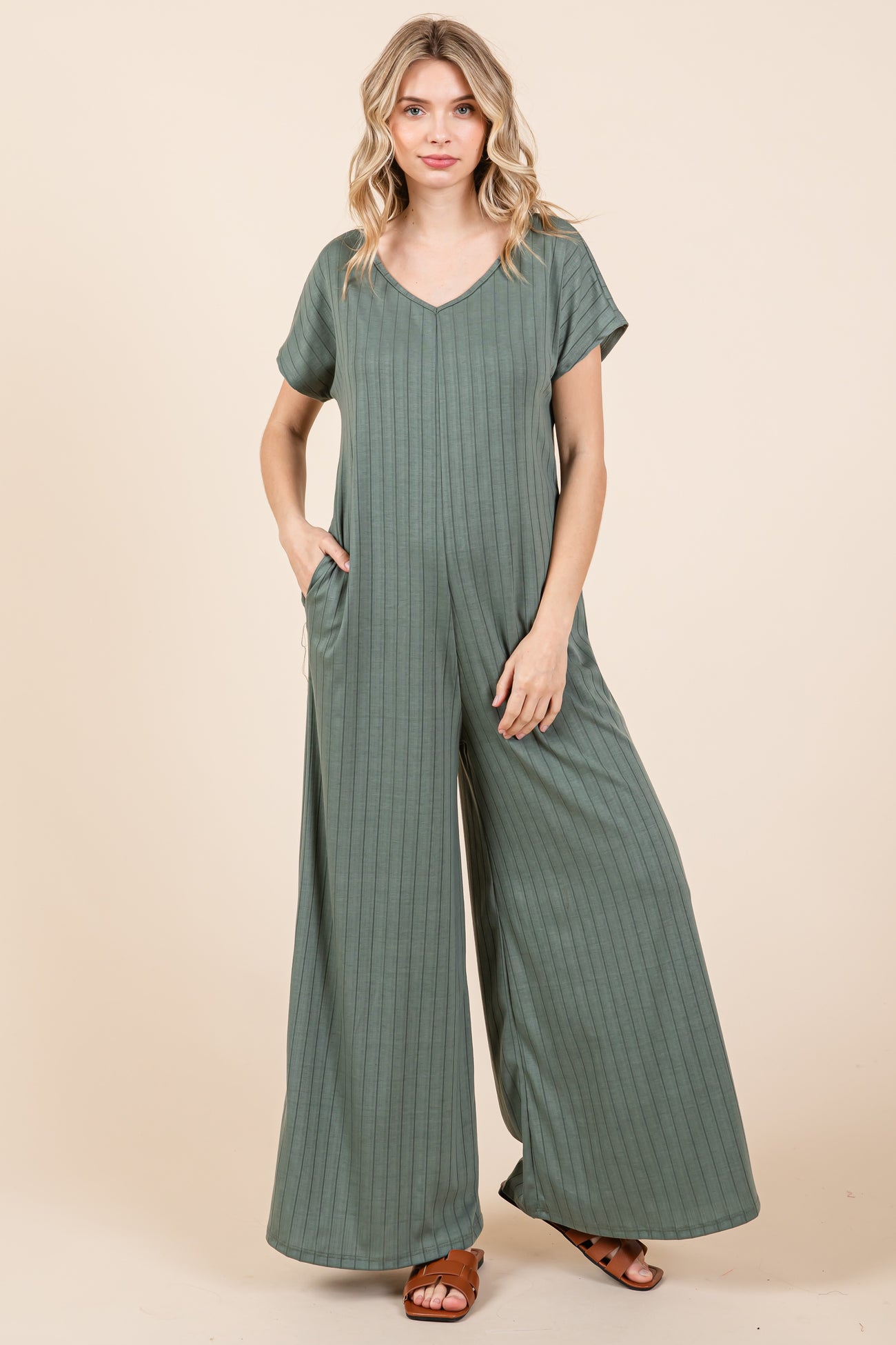woman wearing a green striped short sleeve jumpsuit with pockets and wide legs, styled with brown sandals
