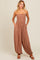 woman wearing a brown patterned jumpsuit with adjustable straps and pockets, styled with brown sandals