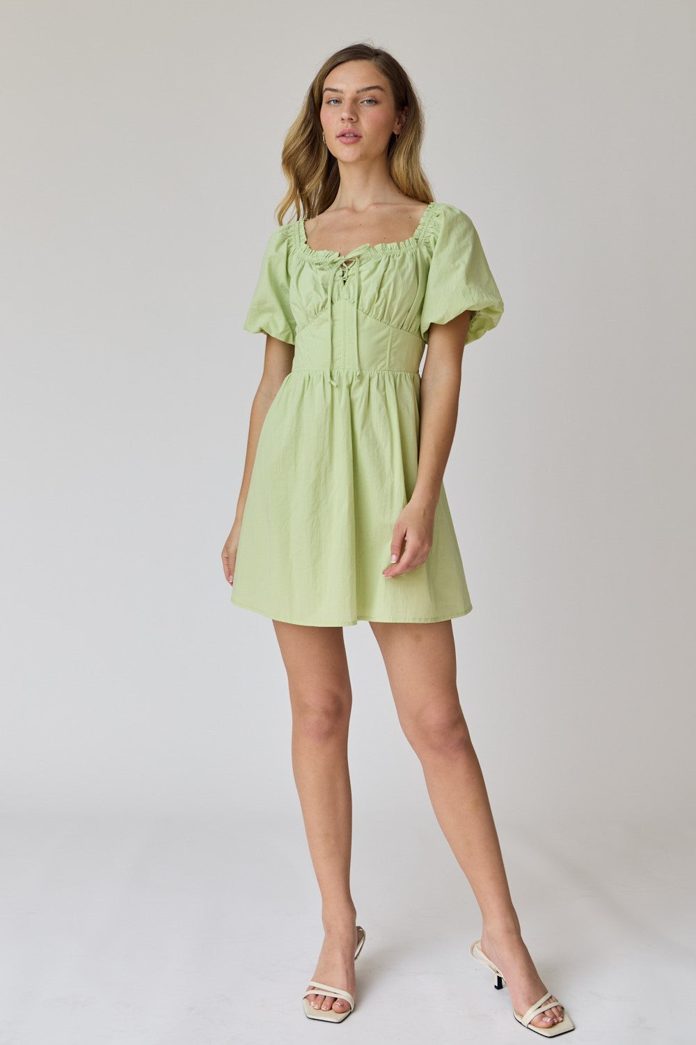 woman wearing a light green short dress with puff sleeves and a lace-up front detail