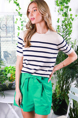 woman wearing a cream and navy striped short sleeve top with green paperbag waist shorts in a floral setting