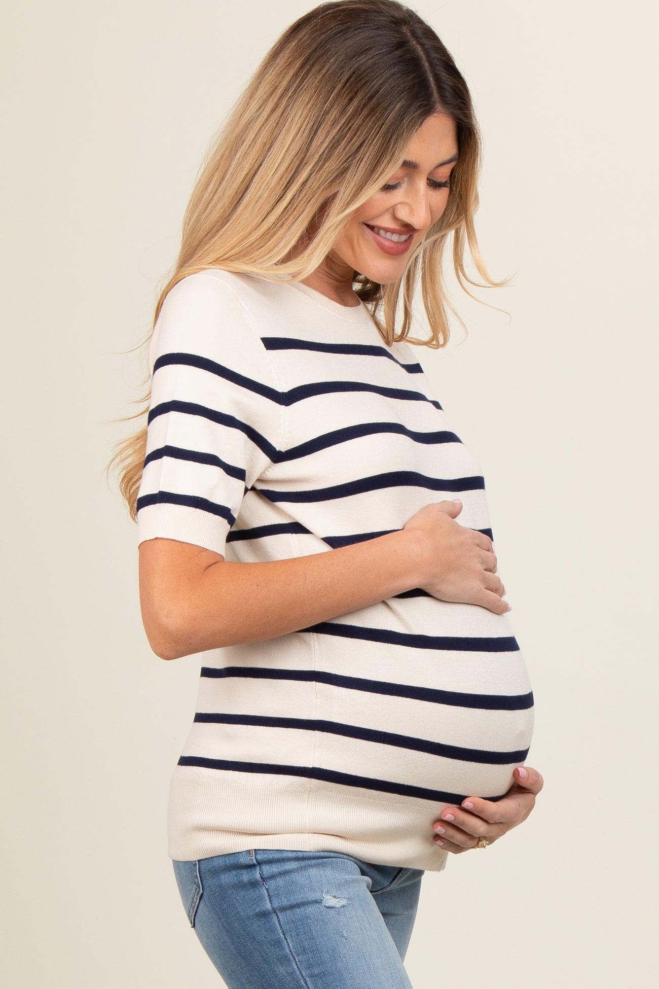 woman wearing a cream and navy striped maternity top and holding her baby bump