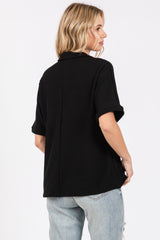 woman wearing a black short sleeve button-up shirt with rolled sleeves and a relaxed fit, seen from the back