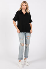 woman wearing a black short sleeve polo top and distressed light wash jeans with rolled cuffs