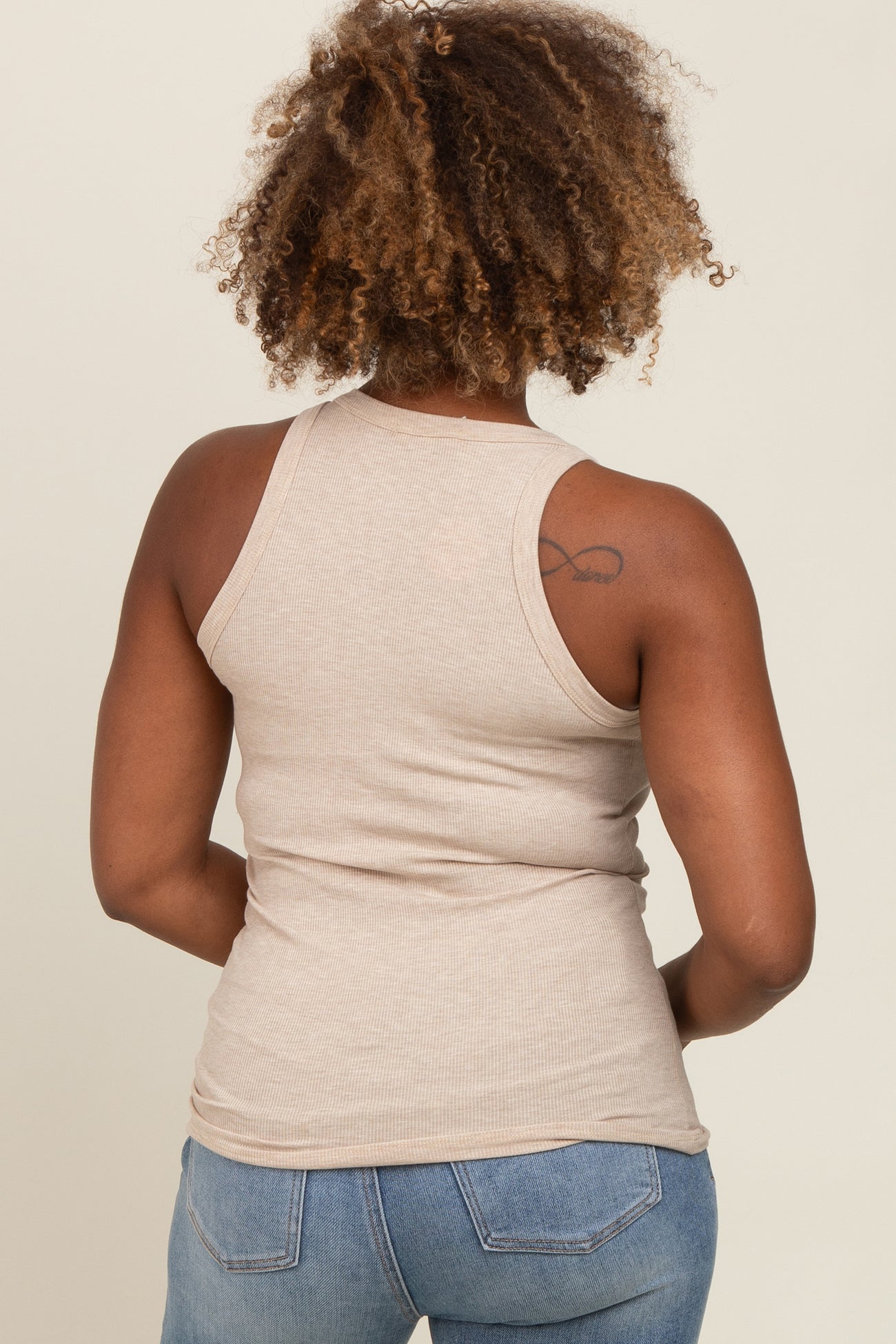 woman wearing a light beige ribbed tank top and blue jeans, seen from the back