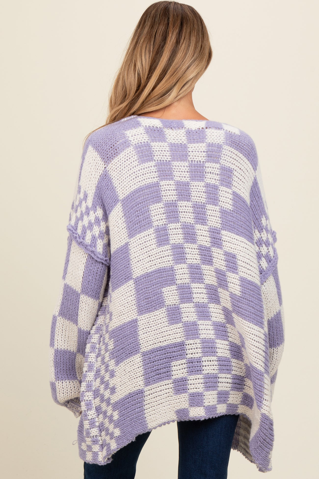 woman wearing a lavender and white checkered maternity sweater with oversized fit and open back detail.