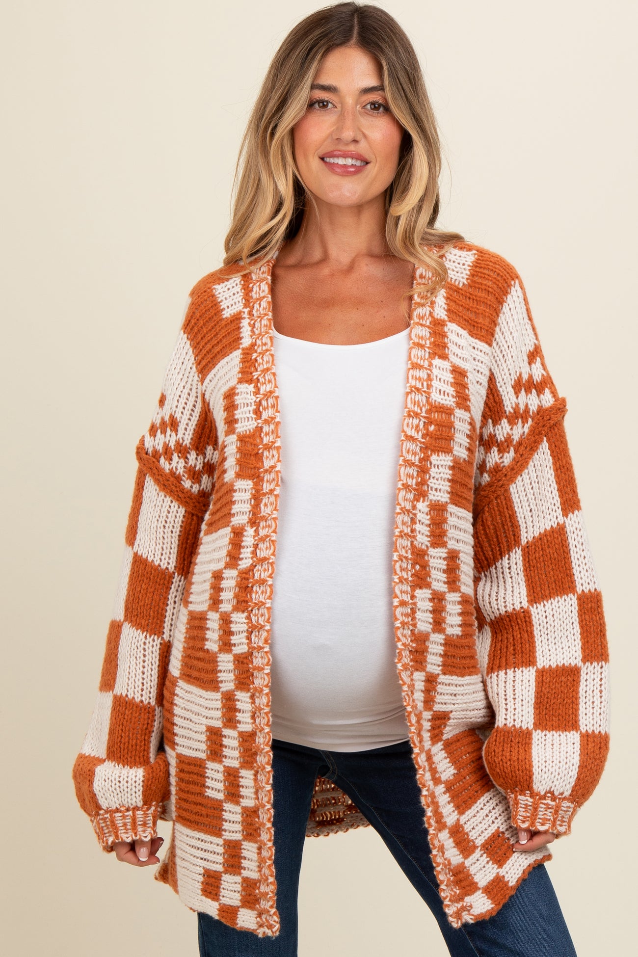 woman wearing an orange and white checkered maternity cardigan over a white top and showing her baby bump