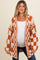 woman wearing an orange and white checkered maternity cardigan over a white top and showing her baby bump